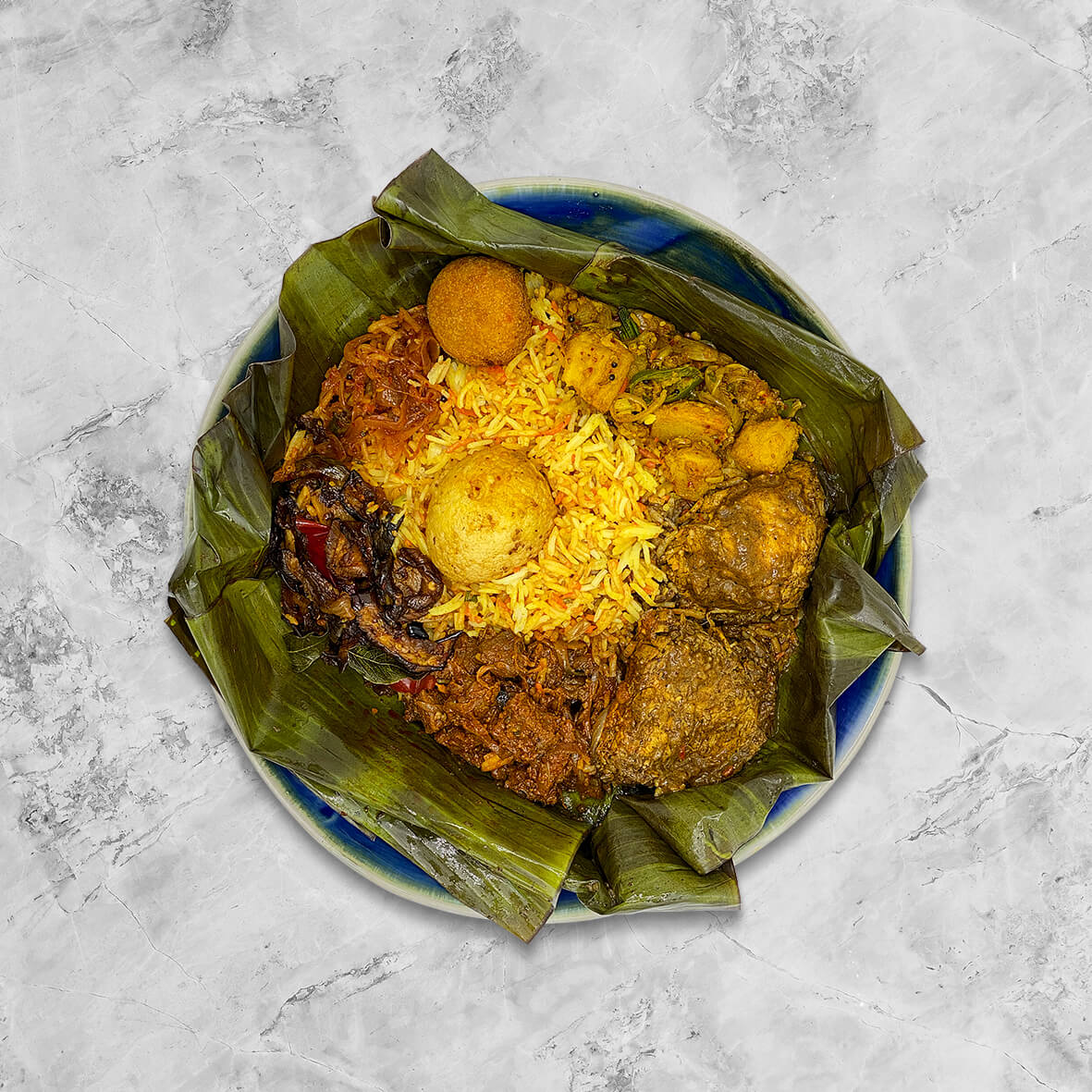 Juicy chunks of mutton & dry chicken curry, tempered potatoes, brinjal moju, fish cutlet and boiled egg with sinni sambol, all wrapped in fragrant banana leaf to seal all that spicy goodness in!